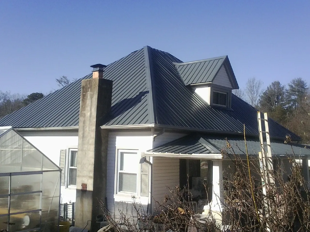 Dark blue standing seam metal roof on a white farmhouse with dormer — Slate & Tile Roof Repair by Roofing Brothers in Buffalo Prairie