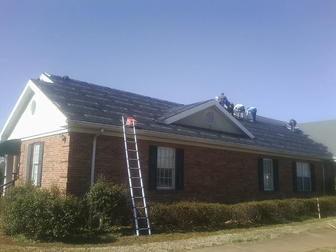 Crew tearing shingles off a brick ranch roof with a ladder set — Metal Roof Repair work by our crew in Buffalo Prairie