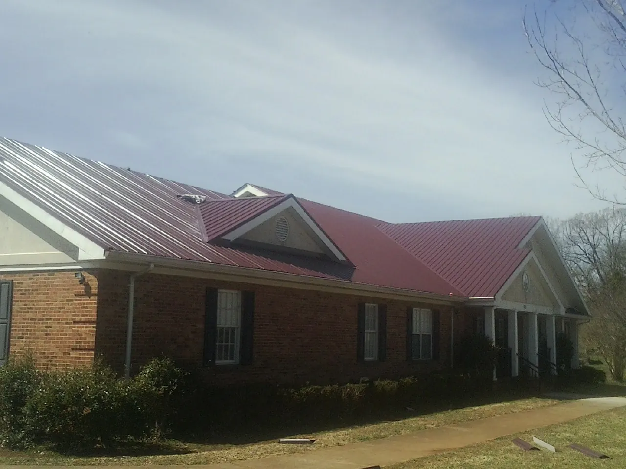 Red metal roof with gabled entries on a long brick building, from a Hail Damage Roof Repair job in Buffalo Prairie