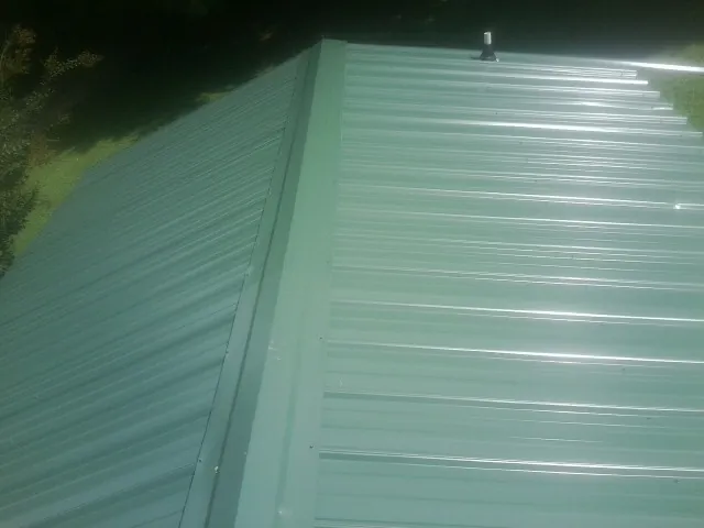 New green metal panels meeting at the ridge of a roof — Flat Roof Repair work by our crew in Buffalo Prairie