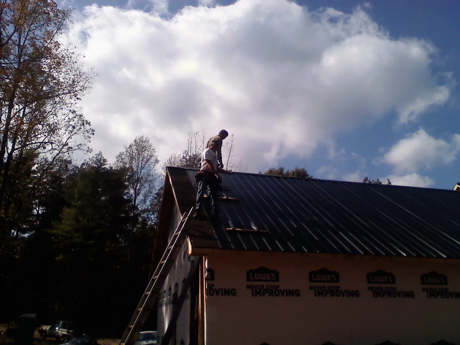 Roofer fastening dark metal panels high against a cloudy sky, from a Roof Inspection job in Buffalo Prairie