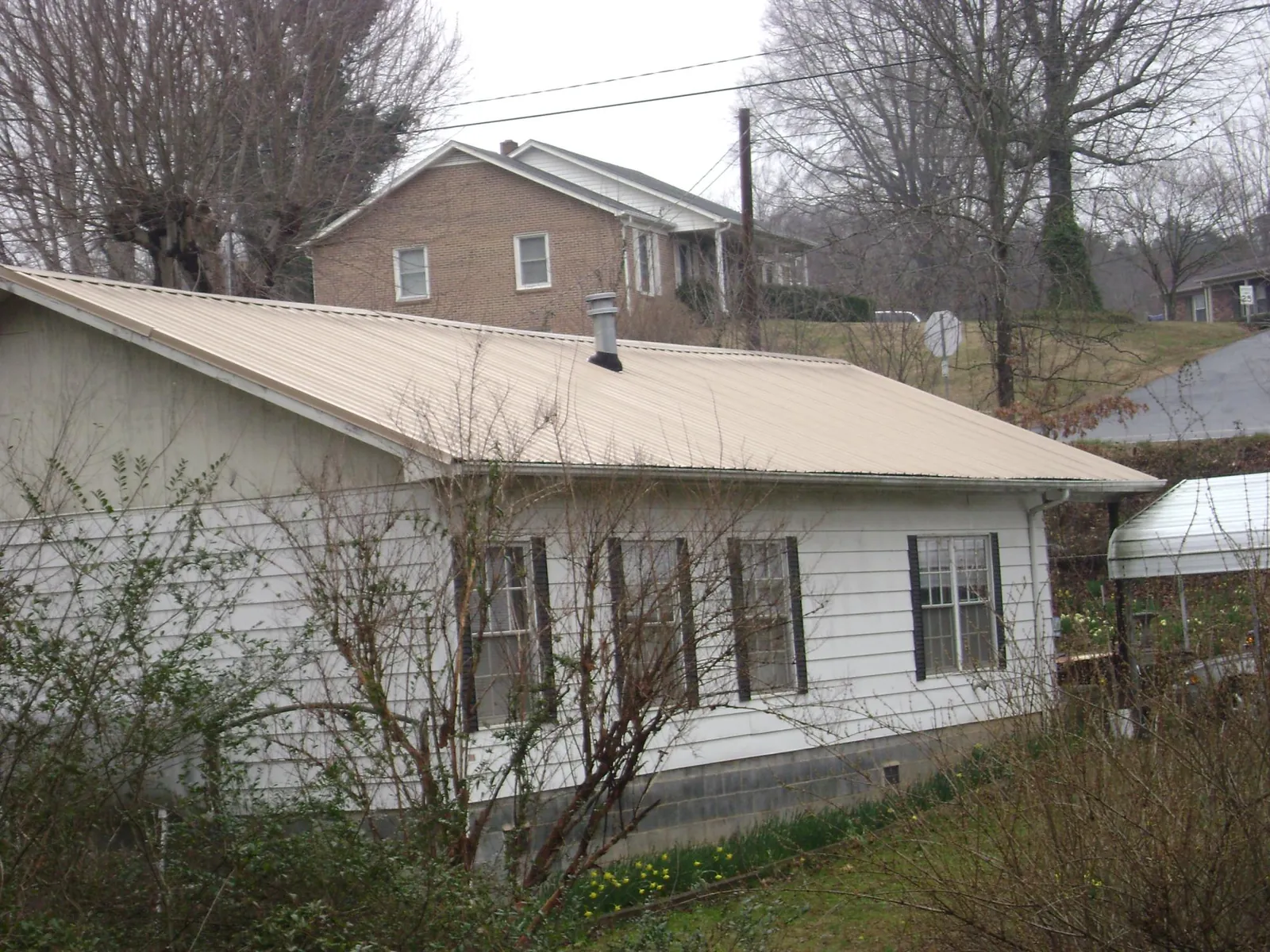 Tan metal roof on a white sided house set into a hillside — Commercial Roofing by Roofing Brothers in Buffalo Prairie