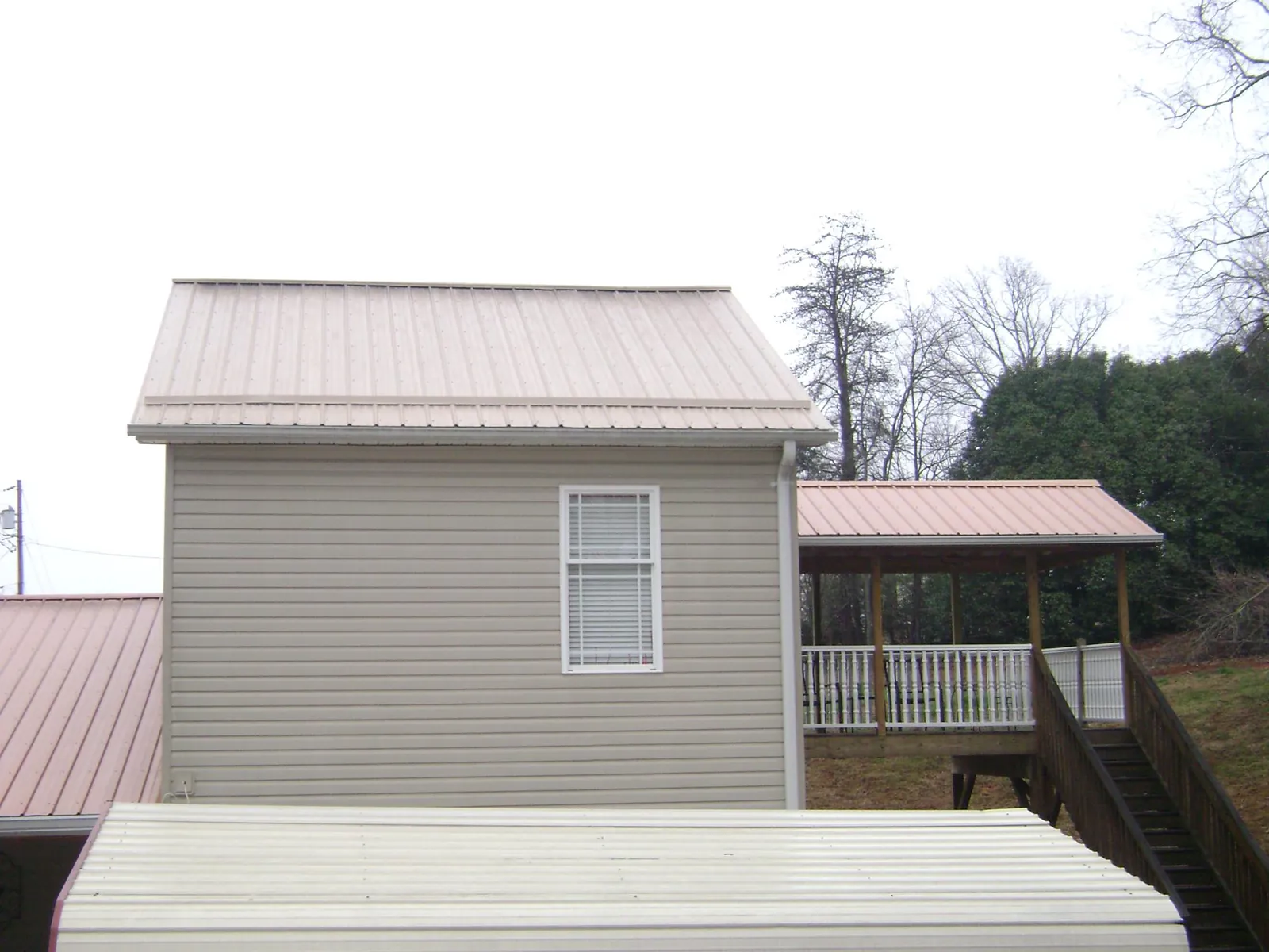 Tan metal roofs on a two story addition and attached porch, from a Roof Replacement job in Buffalo Prairie